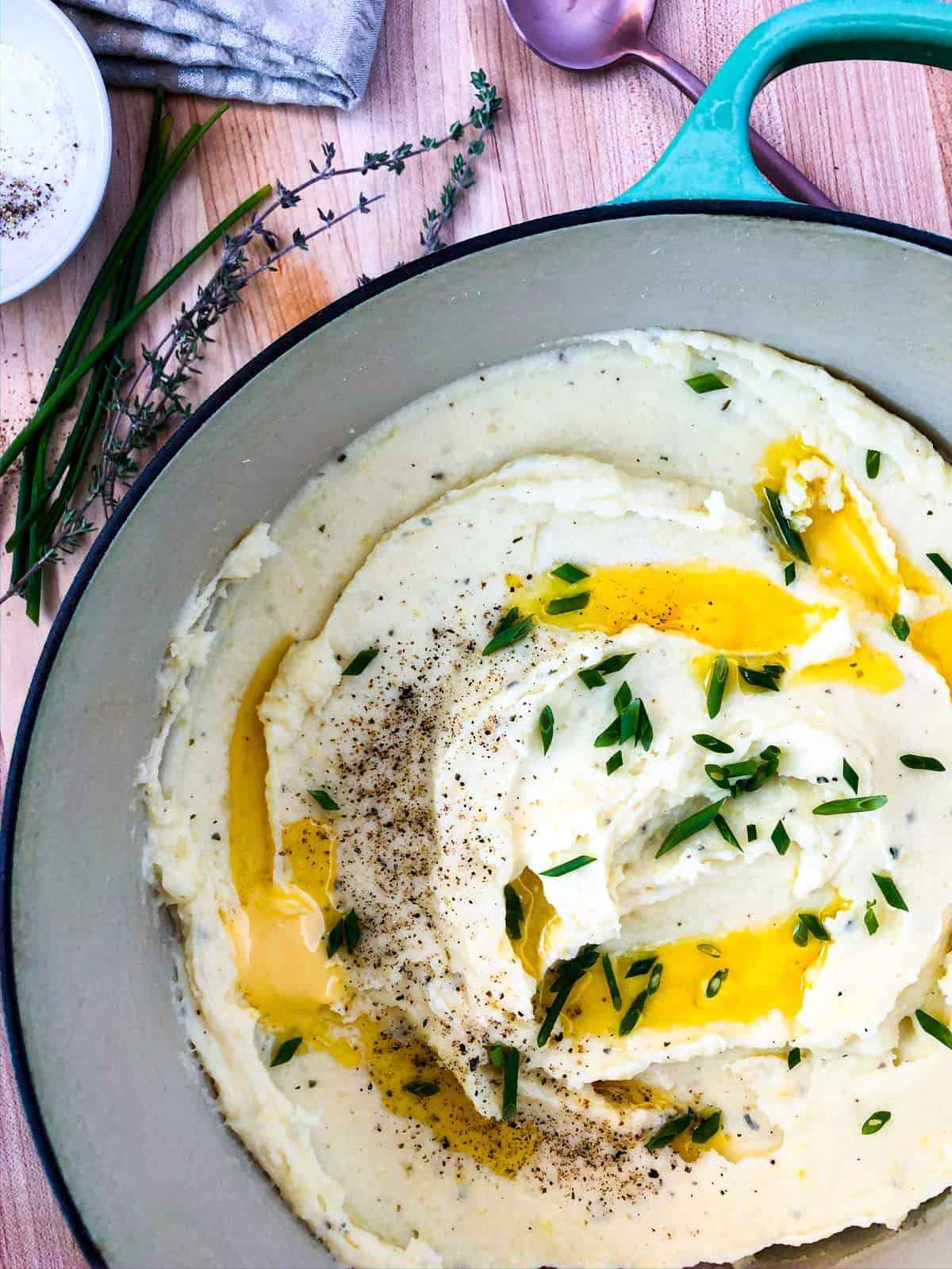 Close up of creamy mashed potatoes garnished with chives, melted butter, and salt and pepper.