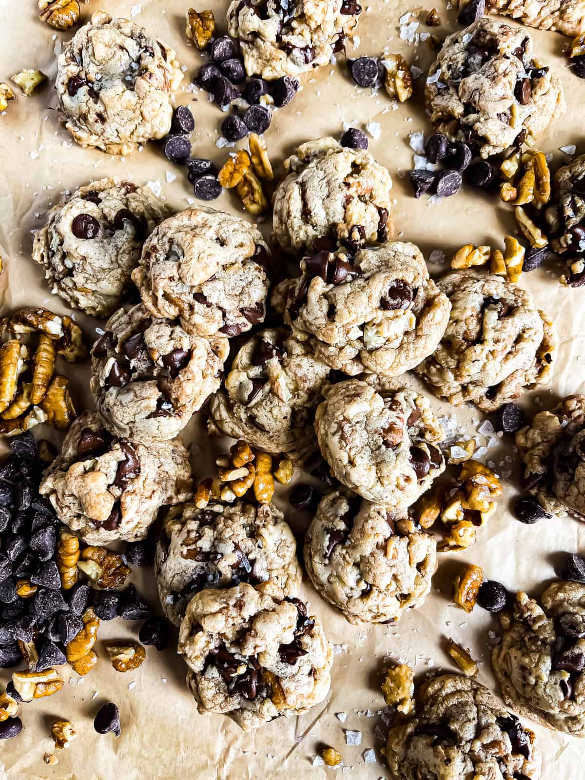 picture of a mound of brown butter chocolate chip cookies with extra pecan and choc chip garnishes