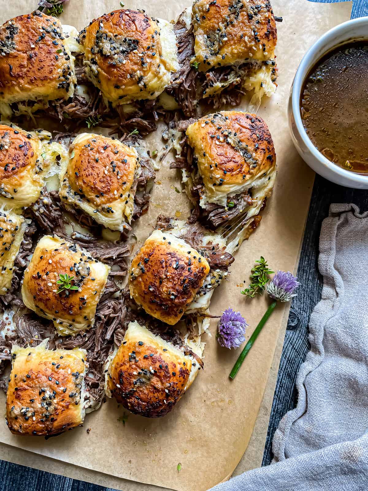 Instant Pot French Dip Sliders, pulled apart and garnished with fresh thyme, chive blossoms, and au jus.
