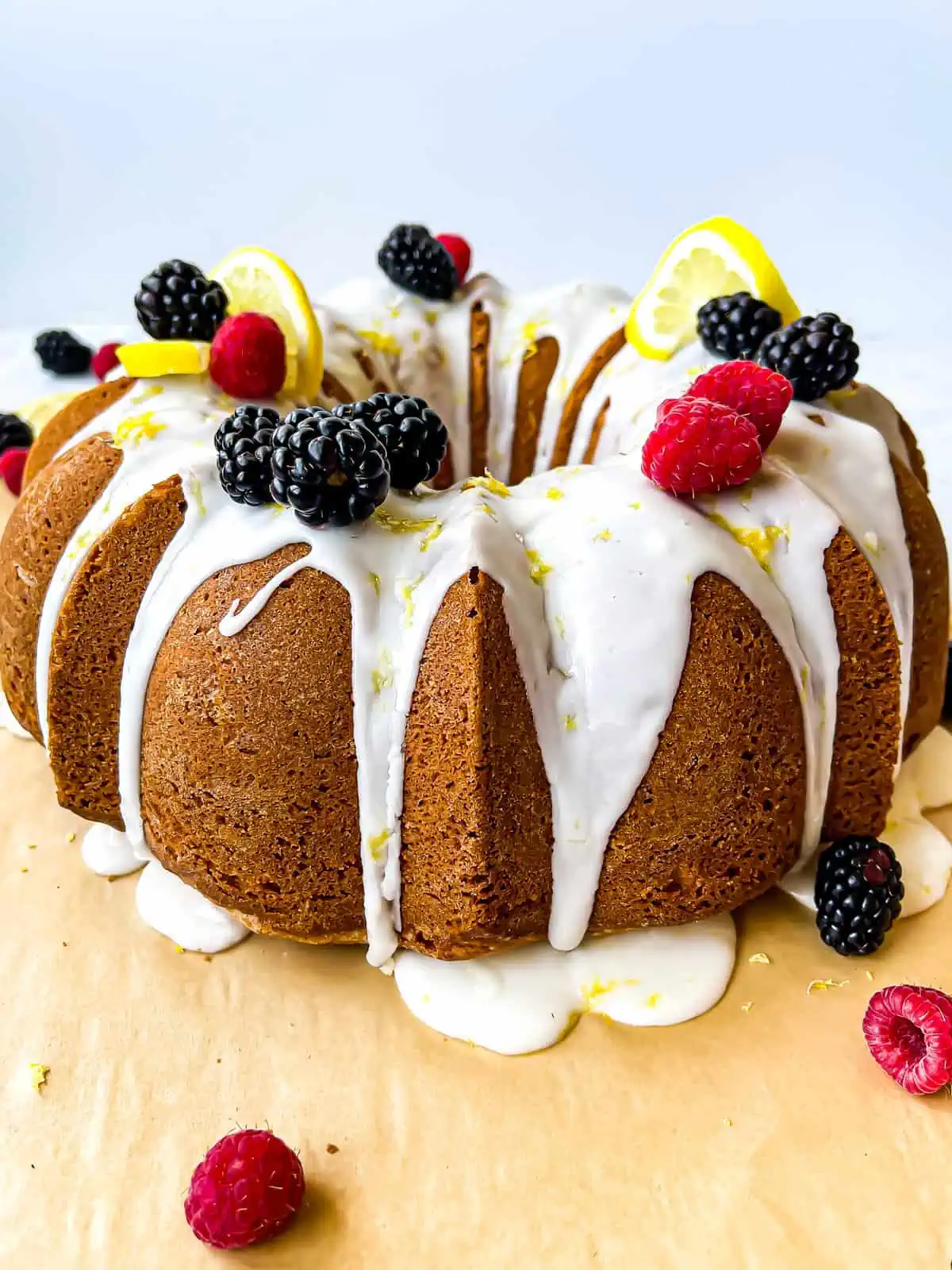 Lemon bundt cake with a lemon glaze, garnished with raspberries, black berries, and lemon slices and zest