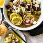 bowl of marinated olives and feta alongside crusty bread for serving and a small side plate of the mixture.