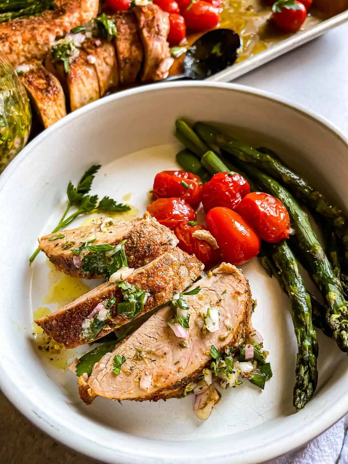 plated sheet pan pork tenderloin with roasted tomatoes and asparagus and chive chimichurri