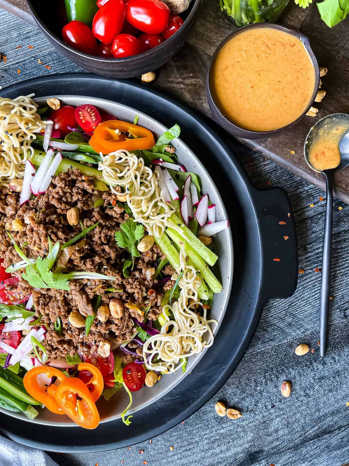 Thai beef salad with peanut dressing. Garnished with fresh veggies, rice noodles, sesame seeds, and extra peanuts