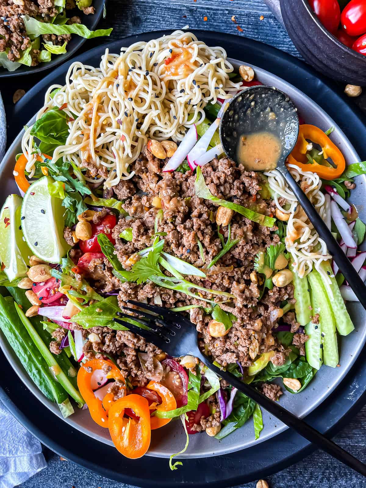 Thai beef salad with peanut dressing. Garnished with fresh veggies, rice noodles, sesame seeds, and extra peanuts