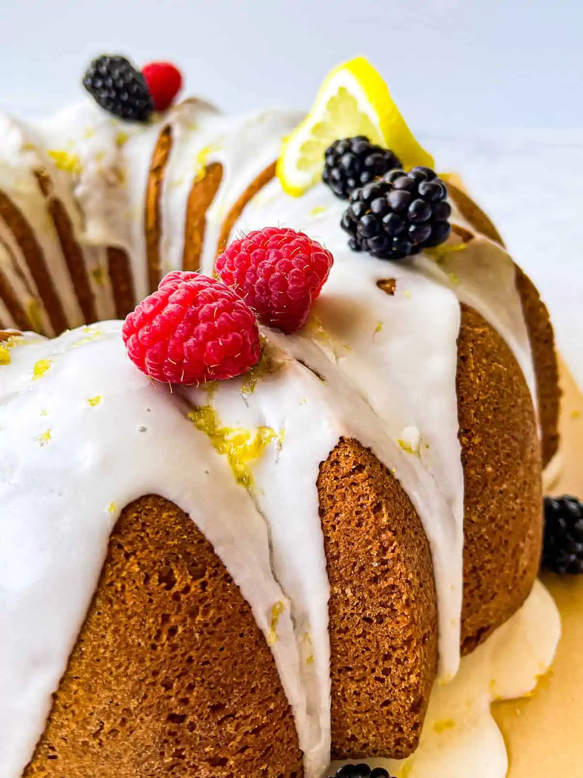 Lemon bundt cake with a lemon glaze, garnished with raspberries, black berries, and lemon slices and zest