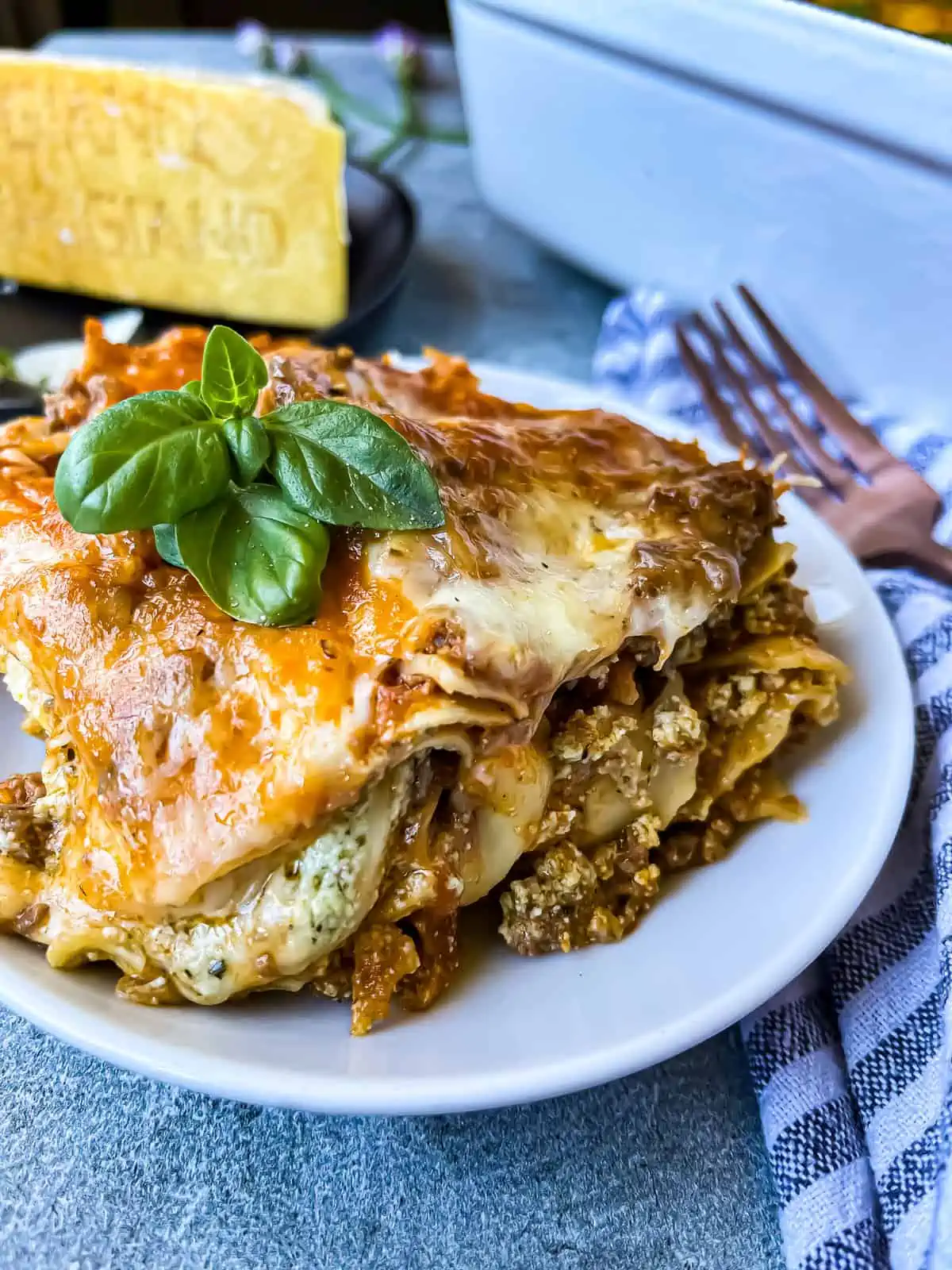 single serving of creamy pesto ricotta lasagna with parmesan wedge in the background