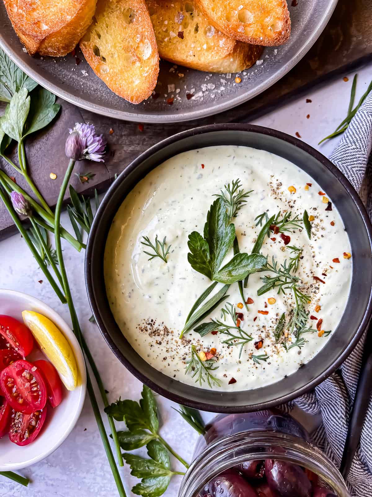 bowl of ricotta dip with fresh herbs, side of crostini and fresh veggies