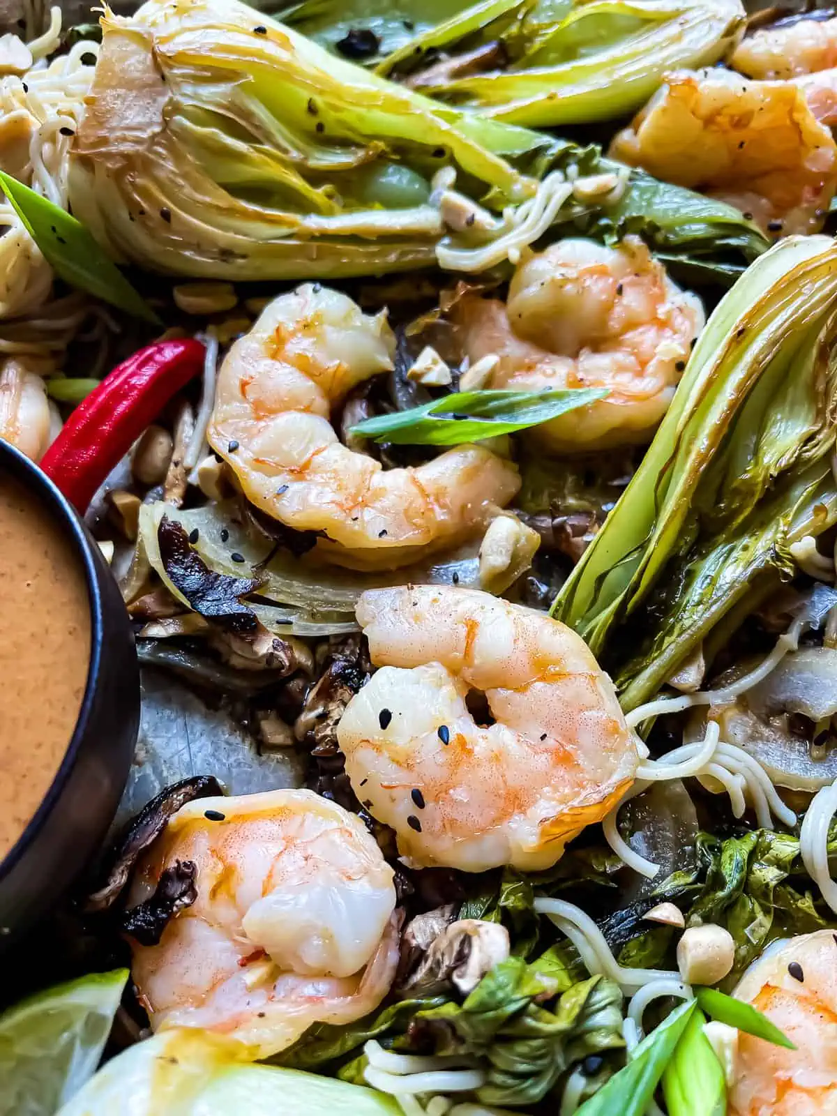 closeup of Asian shrimp, bok choy, and mushrooms on a sheet pan with a side of peanut ginger sauce