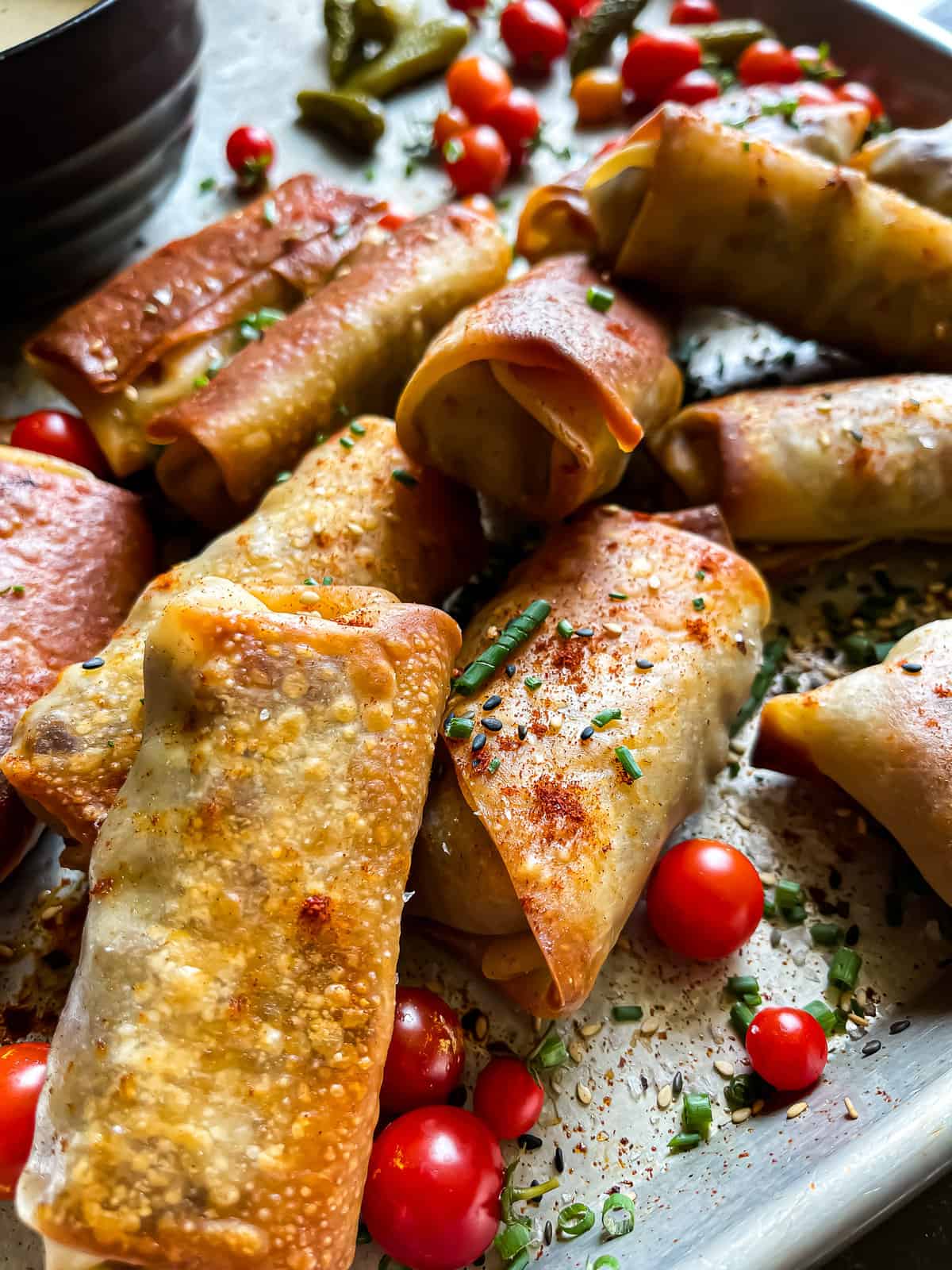 egg rolls garnished with sesame seeds, herbs, spices, and cherry tomatoes