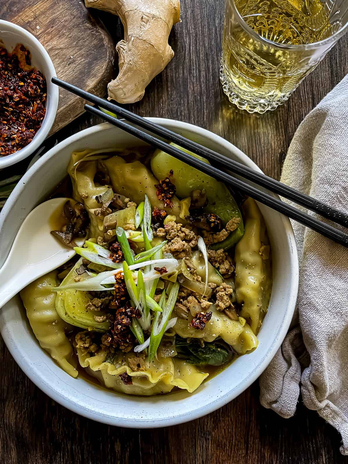 bowl of pork wonton soup, garnished with chili crisp and green onions