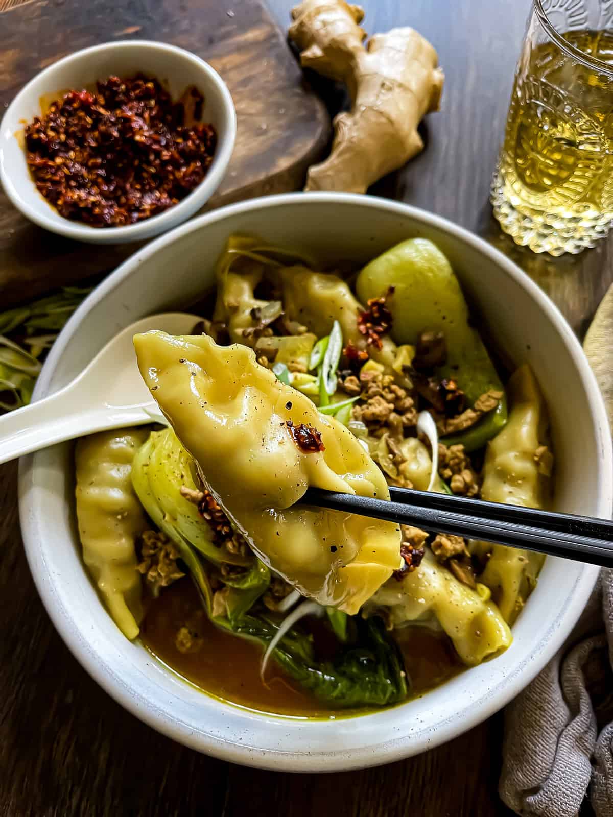 A bowl of wonton soup with a pair chopsticks holding a wonton over the bowl.