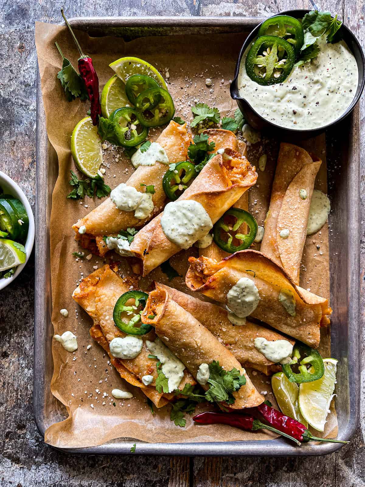 chicken taquitos on a baking sheet drizzled with avocado jalapeno ranch