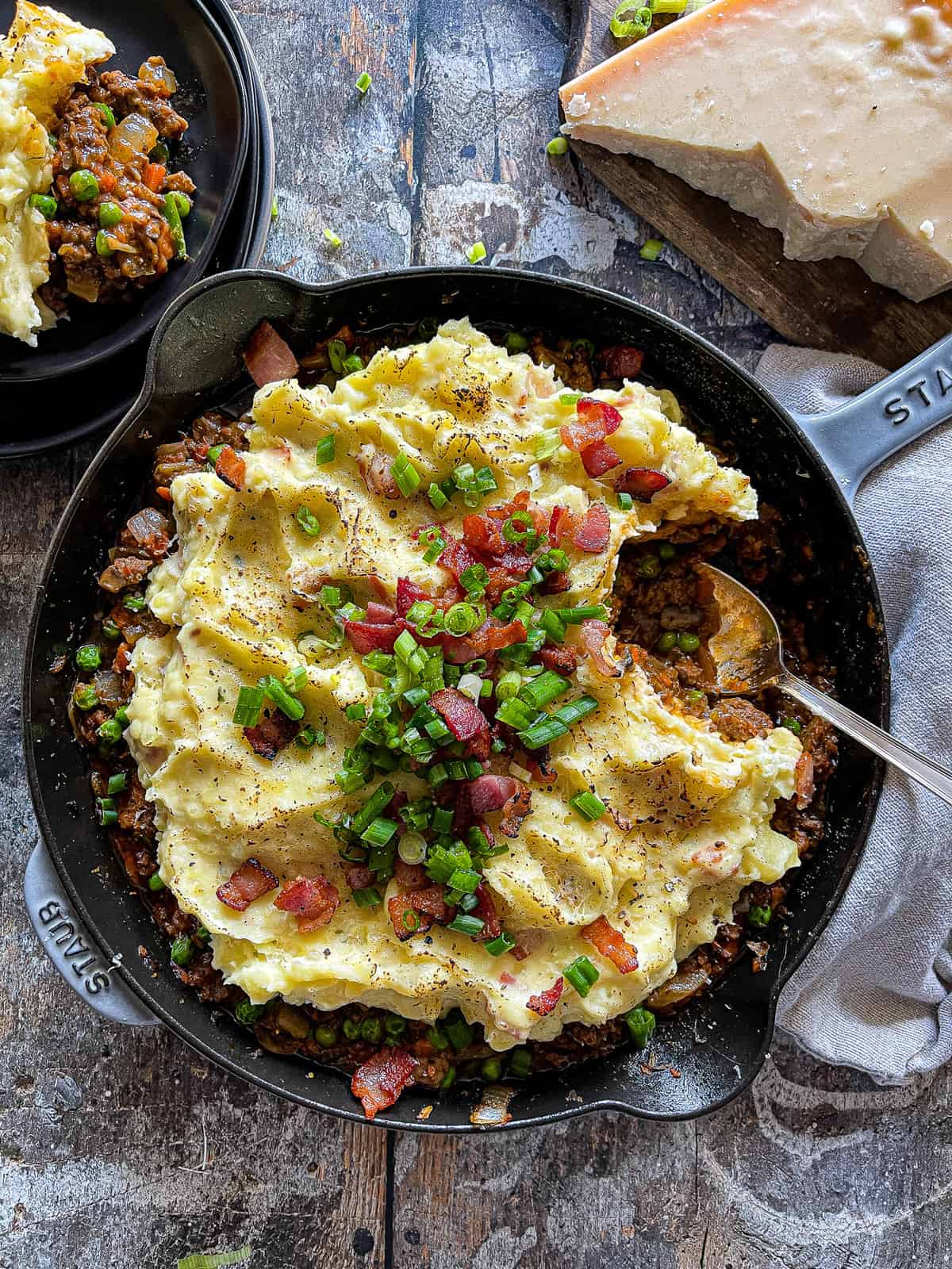 beef shepherd's pie in a large skillet with green onion and bacon garnish