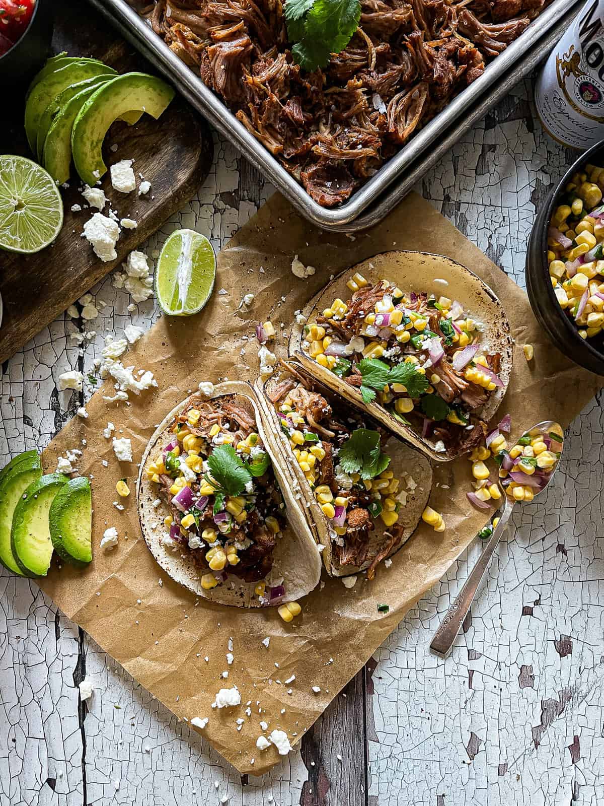 carnitas tacos prepped alongside sweet corn salsa, avocado and lime garnishes