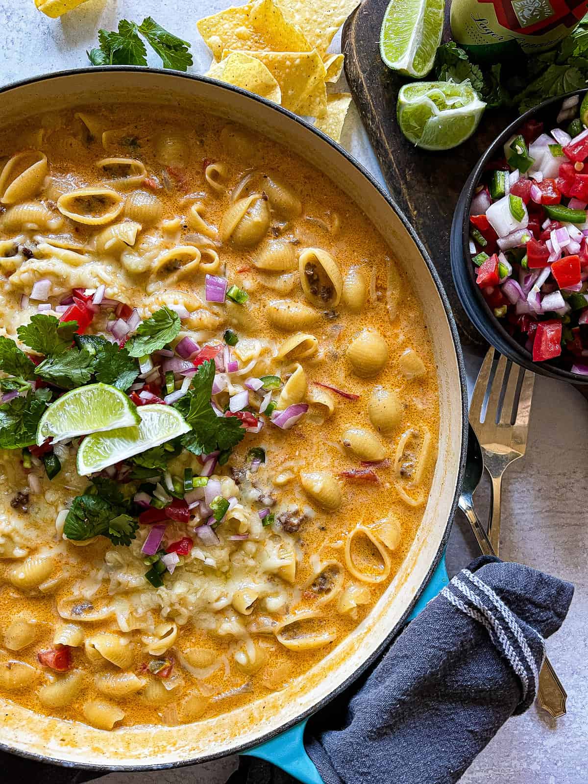 pasta shells cooked in cheese sauce with ground beef garnished with cilantro, pico de gallo, and fresh limes