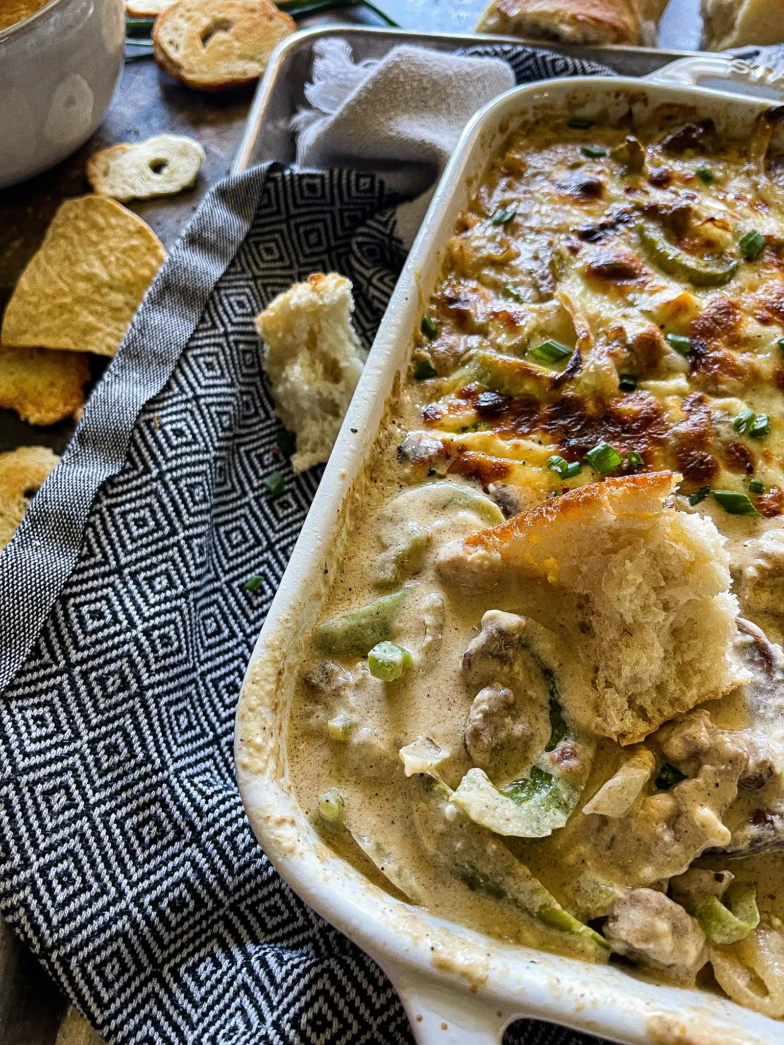 philly cheesesteak dip in a baking dish and garnished with chips and crusty bread for dipping