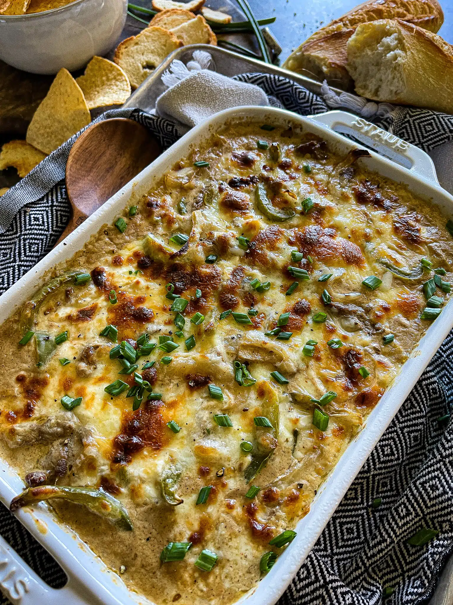 philly cheesesteak dip in a baking dish and garnished with chips and crusty bread for dipping