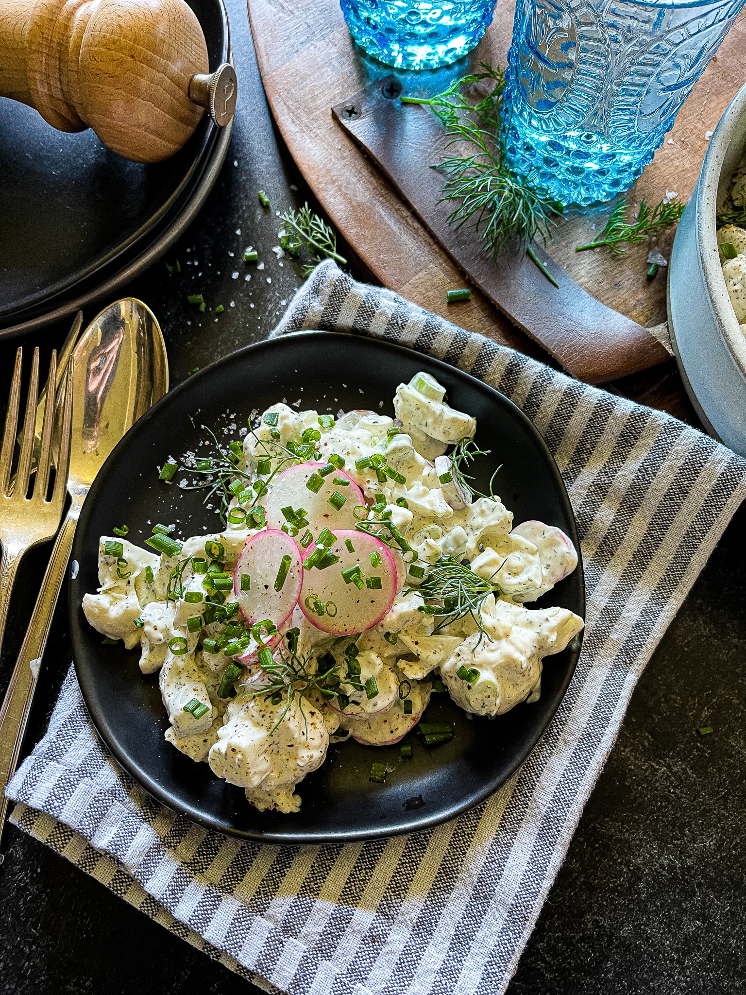 radish salad with cauliflower and green onion, garnished with chives and dill, in a serving bowl