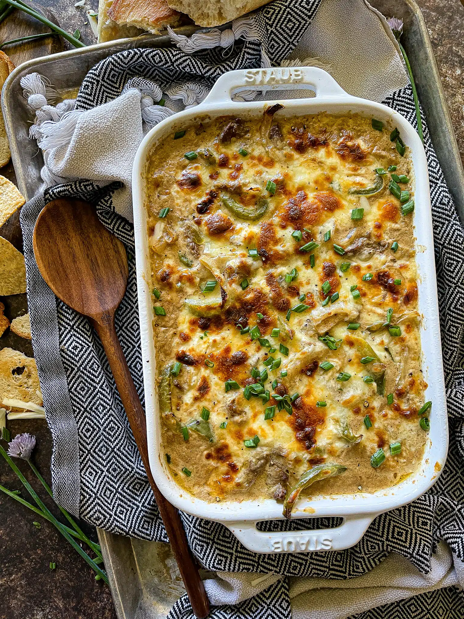 philly cheesesteak dip in a baking dish and garnished with chips and crusty bread for dipping