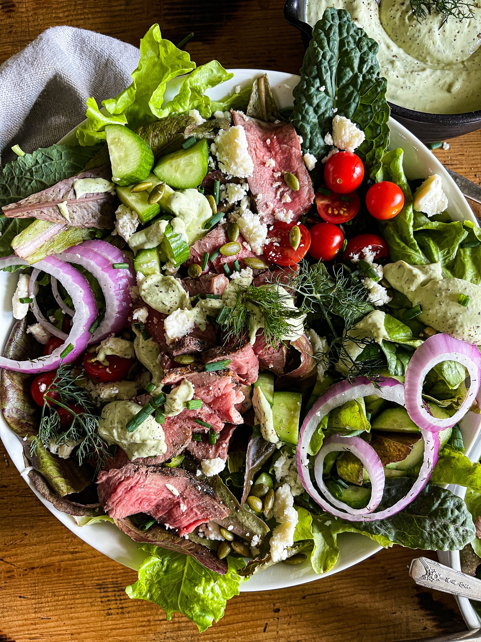 bowl of mixed greens, steak, tomatoes, pickled onions, cucumbe, pepitas, queso fresco and avocado ranch dressing