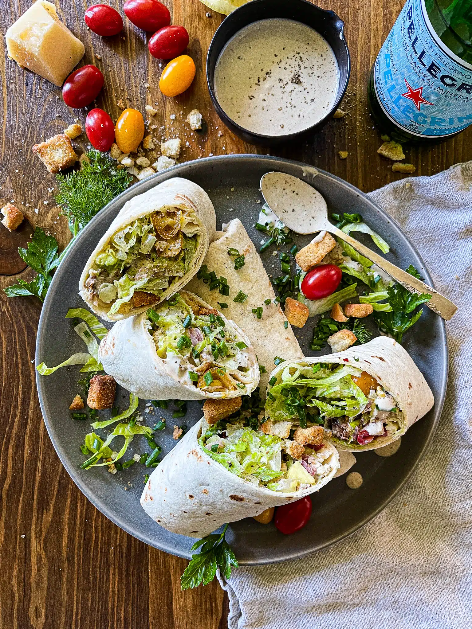 chicken caesar salad wraps on a serving plate with a bottle of pellegrino, extra dressing, and garnishes