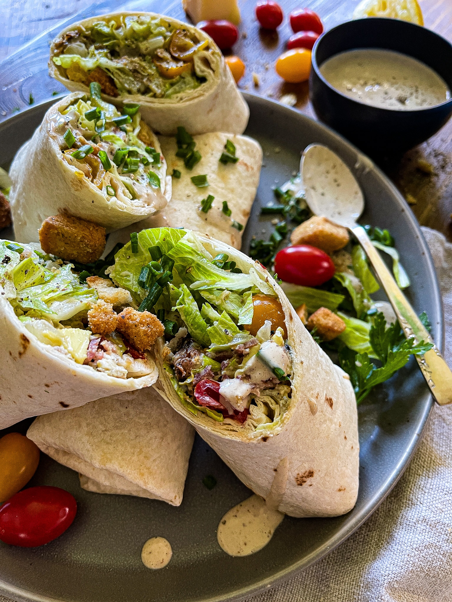 halved chicken caesar salad wraps on a plate with extra dressing and garnishes