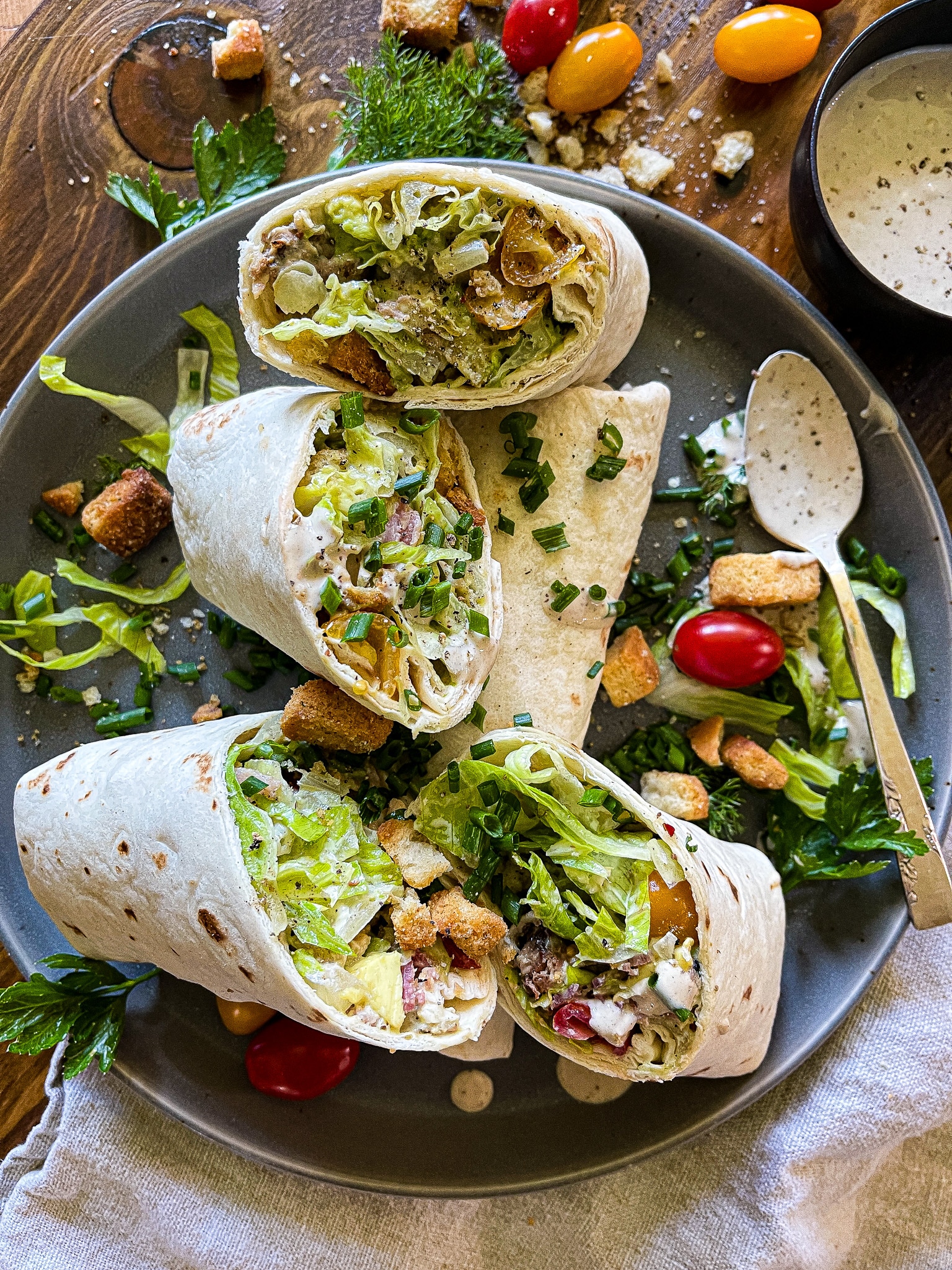 chicken caesar salad wraps on a serving plate with a bottle of pellegrino, extra dressing, and garnishes