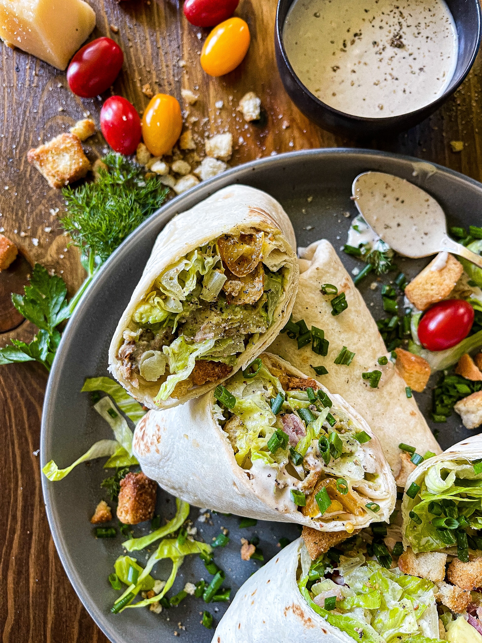 chicken caesar salad wraps on a serving plate with a bottle of pellegrino, extra dressing, and garnishes
