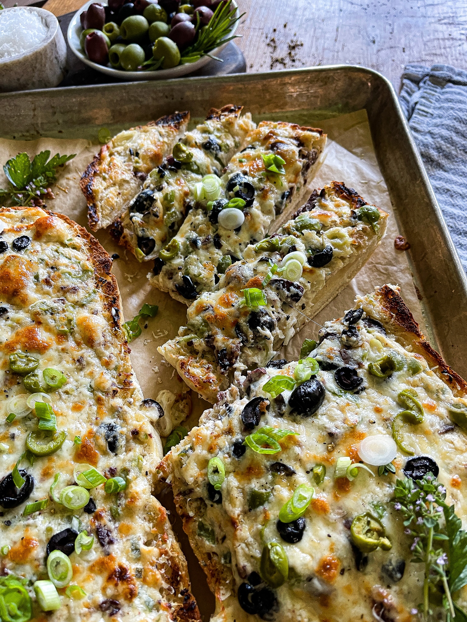 a halved loaf of French bread, with the olive cheese bread spread, served on a parchment line baking sheet