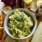 avocado egg salad on a toasted everything bagel above a cutting board with the recipe ingredients and equipment