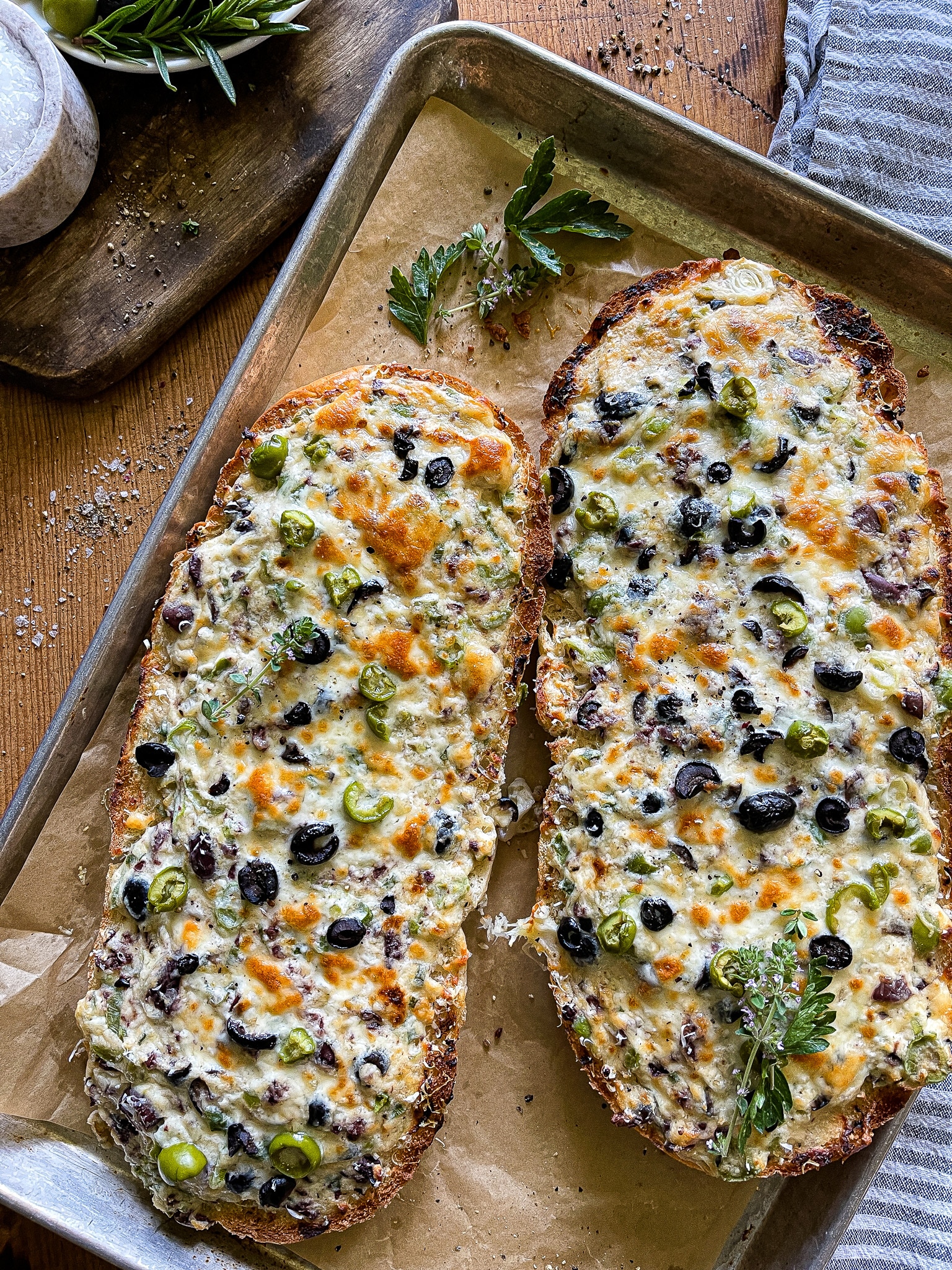 a halved loaf of French bread, with the olive cheese bread spread, served on a parchment line baking sheet