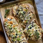 a halved loaf of French bread, with the olive cheese bread spread, served on a parchment line baking sheet