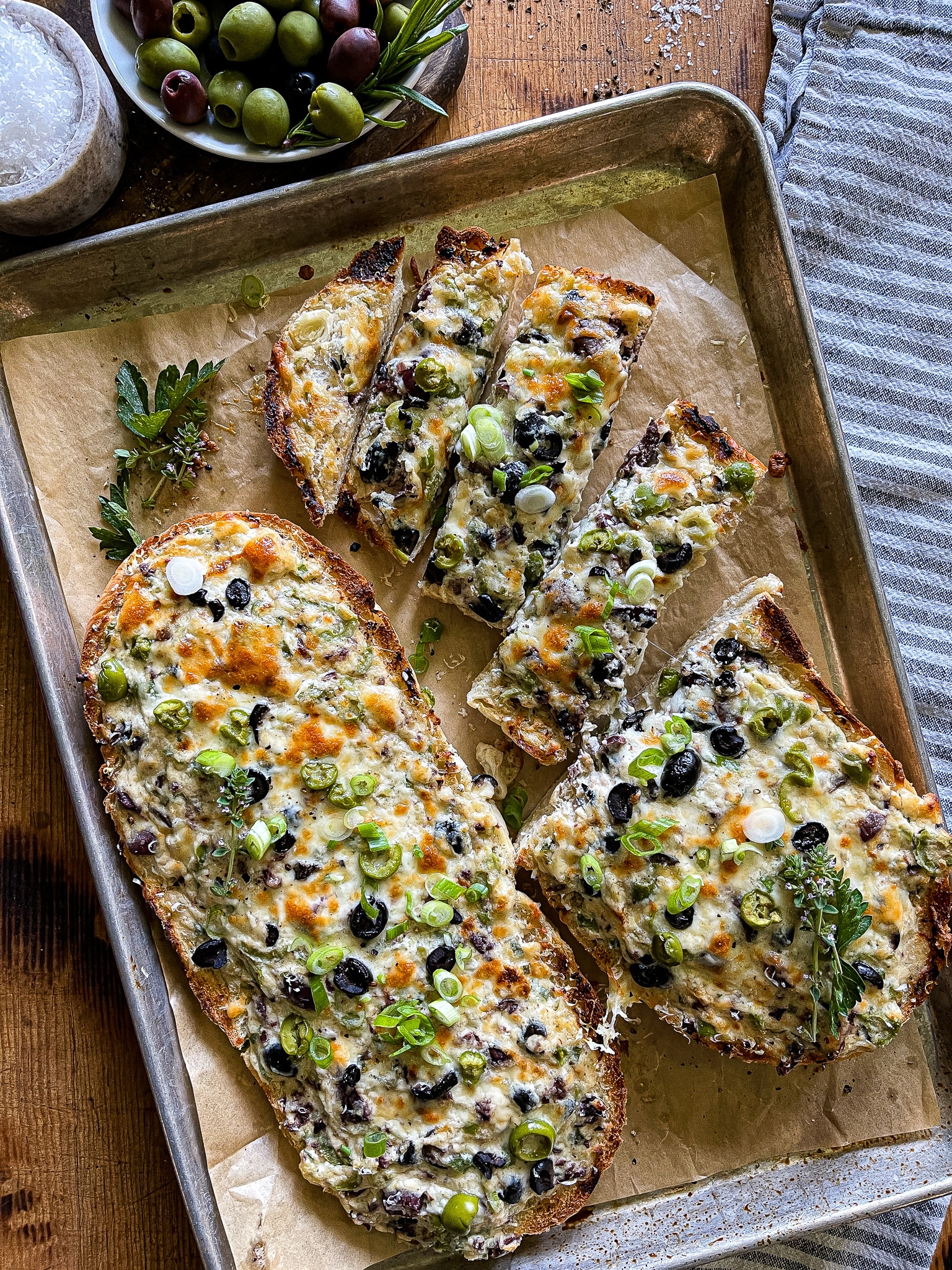 a halved loaf of French bread, with the olive cheese bread spread, served on a parchment line baking sheet