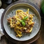 pasta alla genovese served on a plate from a dutch oven, garnished with parmesan cheese and fresh herbs