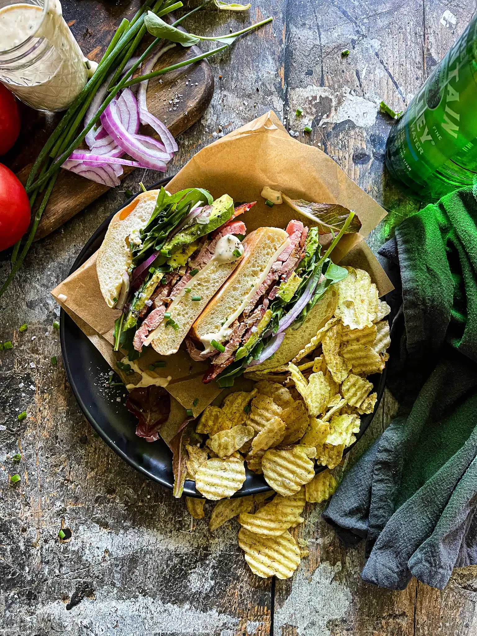 a roasted pork tenderloin sandwich, cut in half, with avocado, bacon, veggies on a plate with a side of dill pickle potato chips - for back to school recipe roundup