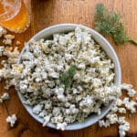 a large bowl of dill pickle popcorn, garnished with fresh dill