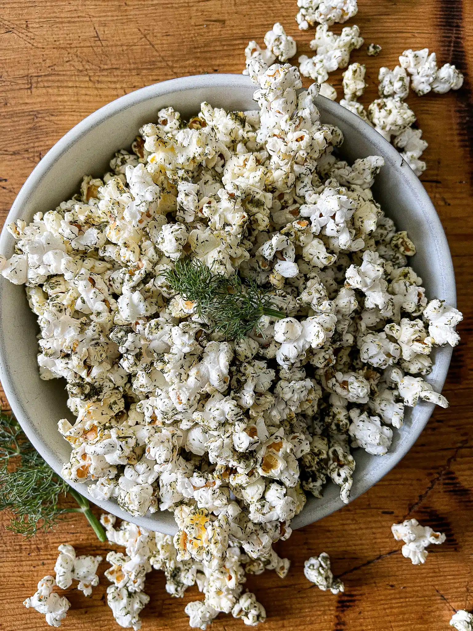 a large bowl of dill pickle popcorn, garnished with fresh dill