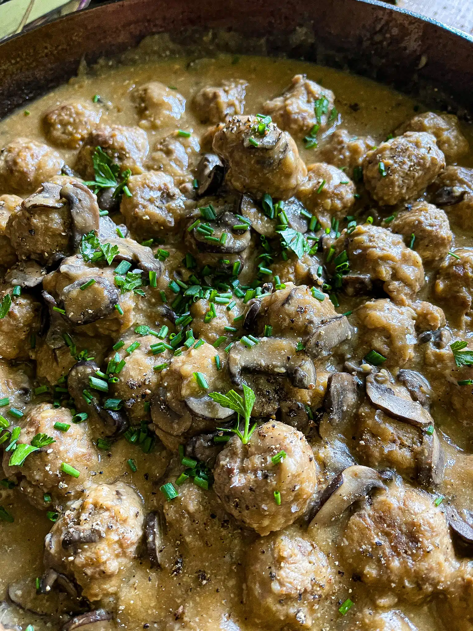 meatballs and mushrooms with gravy, garnished with chives and parsley