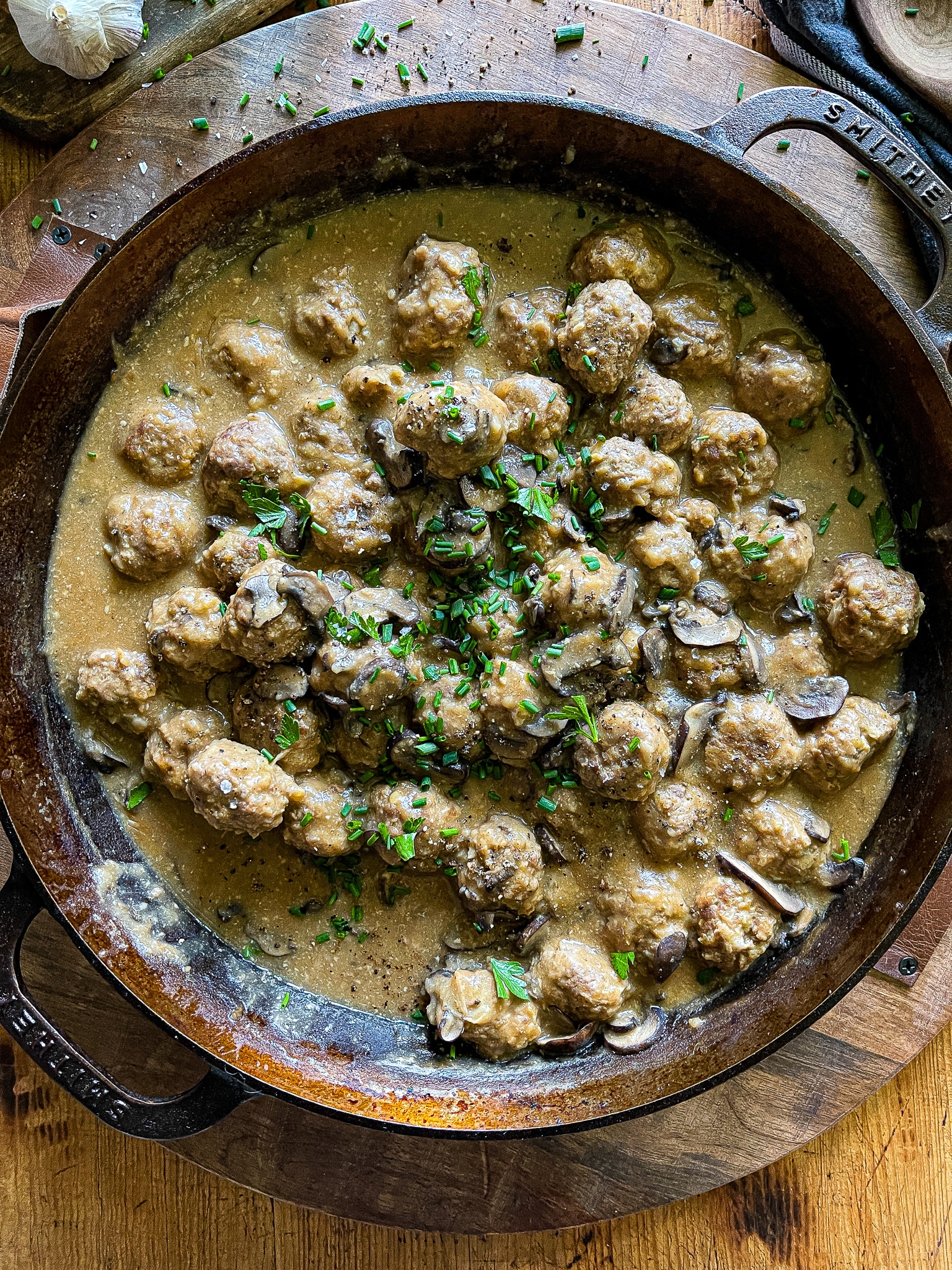 salisbury steak meatballs in a cast iron skillet garnished with chives and parsley