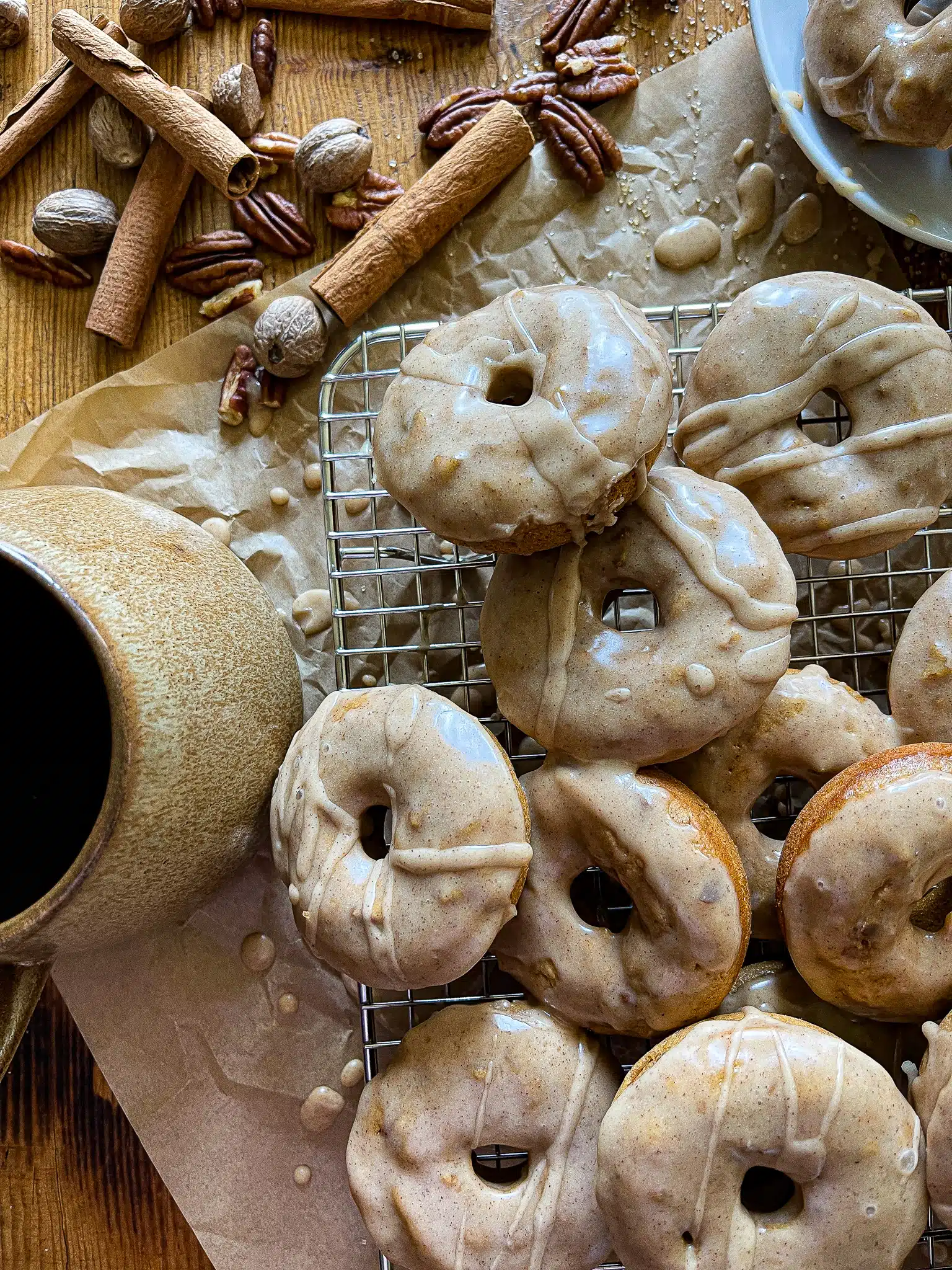 This is a picture of apple cider donuts with a cup of tea, garnished with cinnamon stick and whole nutmeg. 