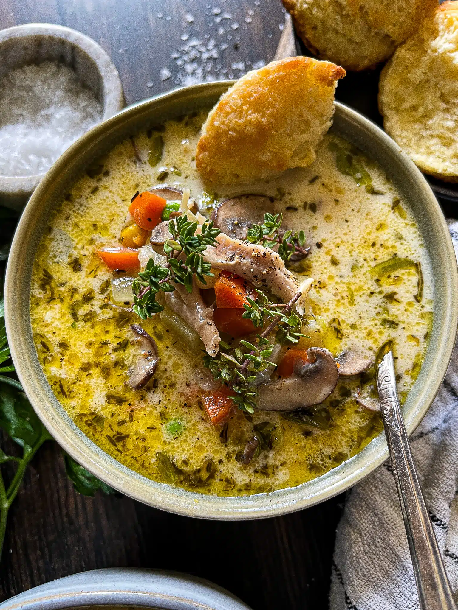 This is a bowl of chicken pot pie soup with a small piece of biscuit for dunking on the side.