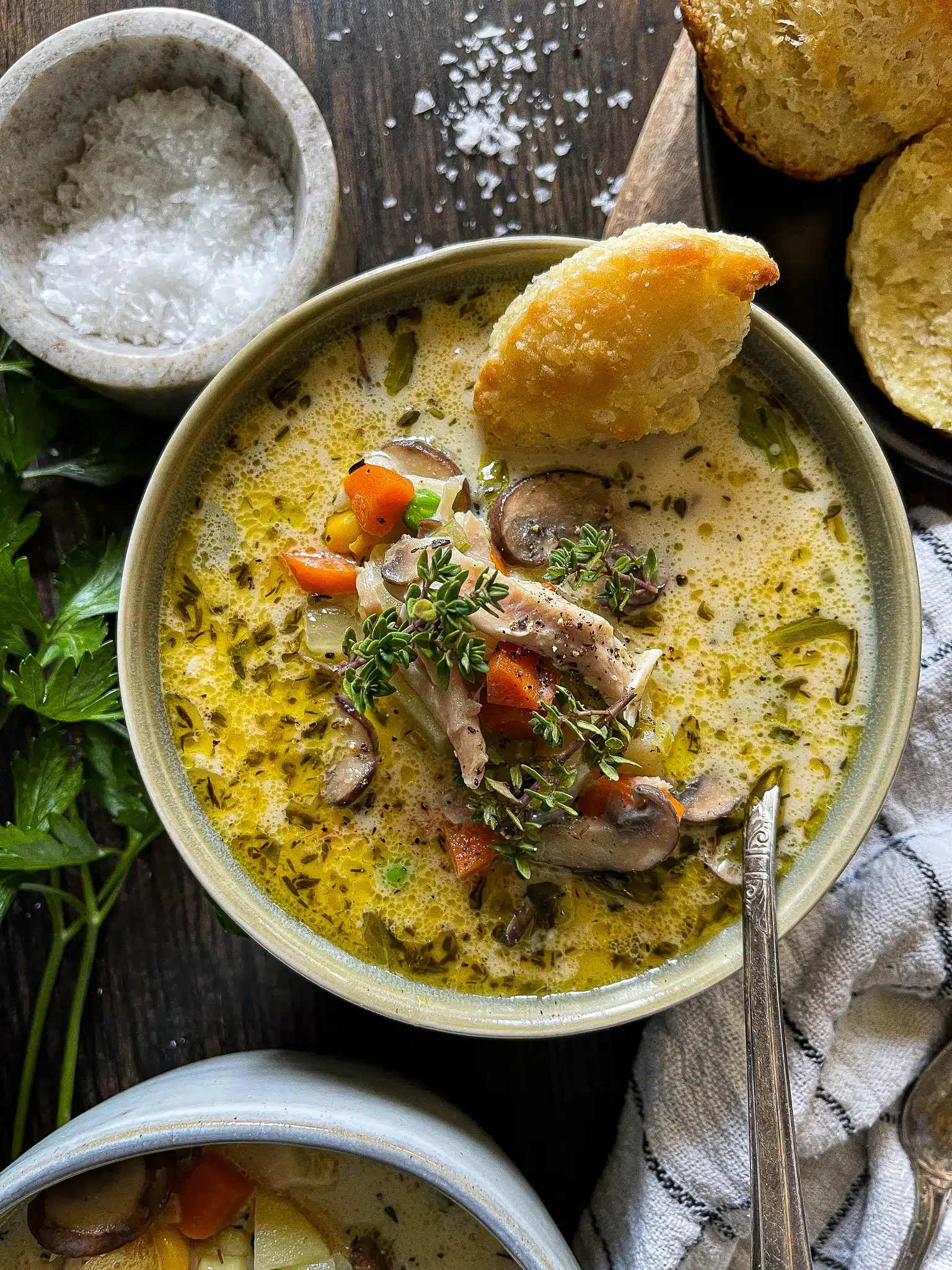 This is a bowl of chicken pot pie soup with a small piece of biscuit for dunking on the side of the bowl. 