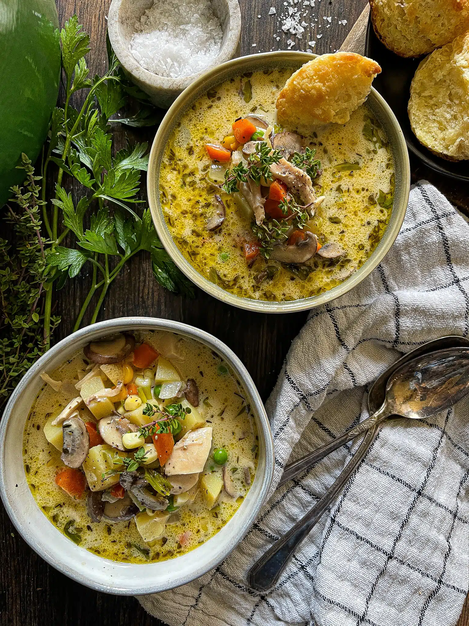 This is a picture of two bowls of chicken pot pie soup with fresh herbs on the side.