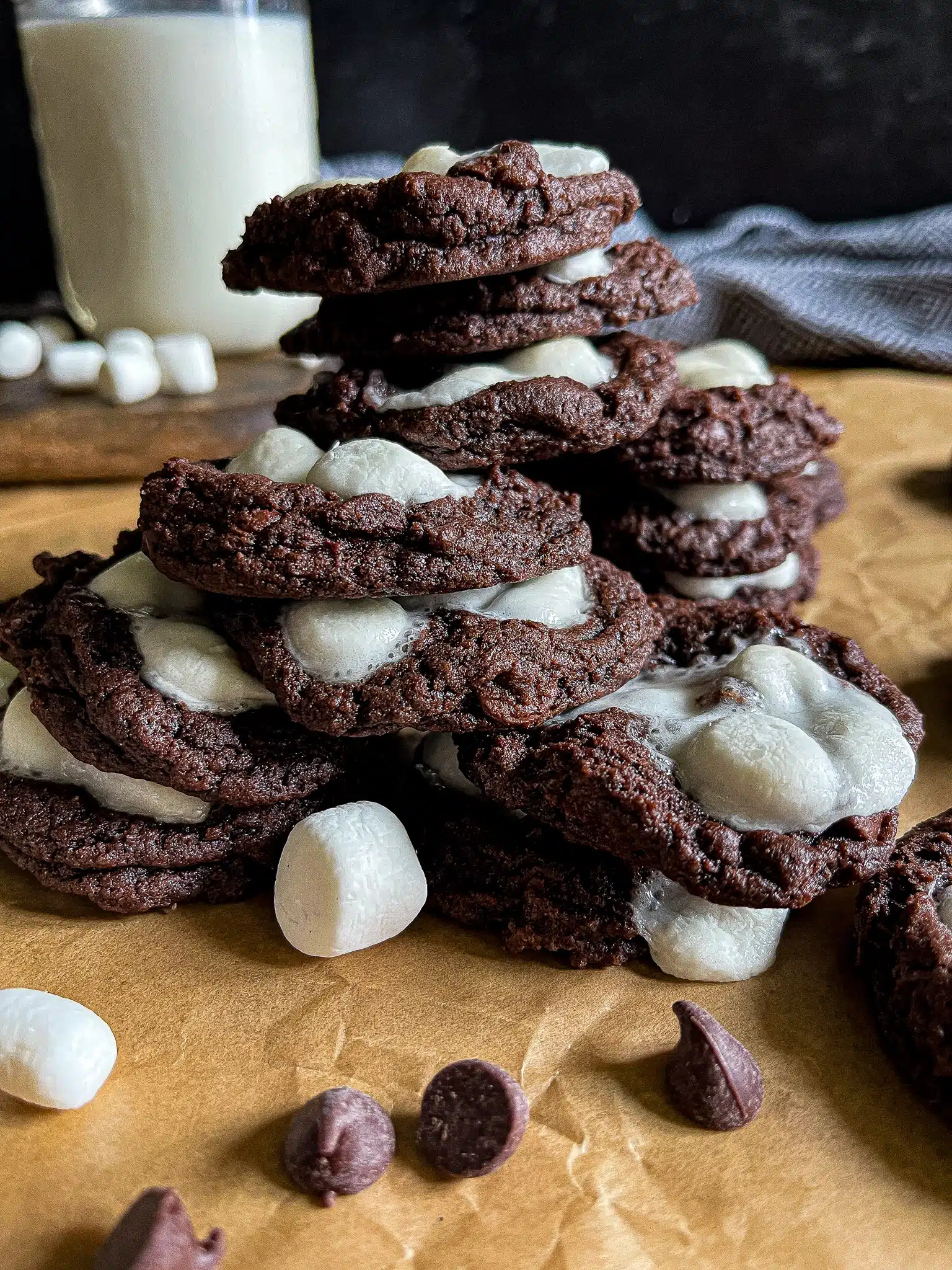 This is a picture of Hot Chocolate Cookies stacked on top of each other with a large glass of milk in the background.