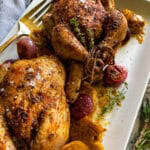 This is a white serving platter with two roasted cornish hens and a vintage serving fork.