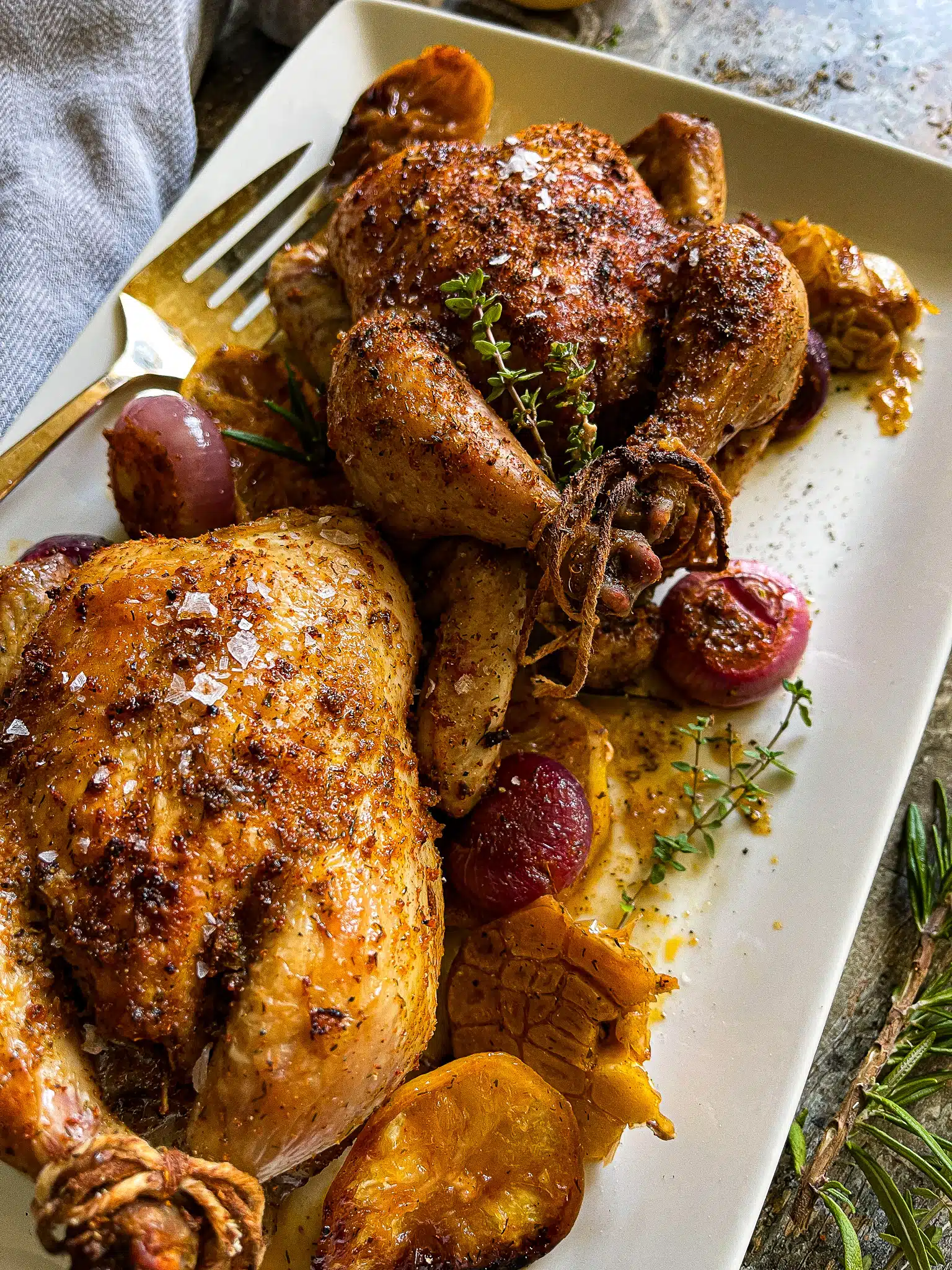 This is a white serving platter with two roasted cornish hens and a vintage serving fork.