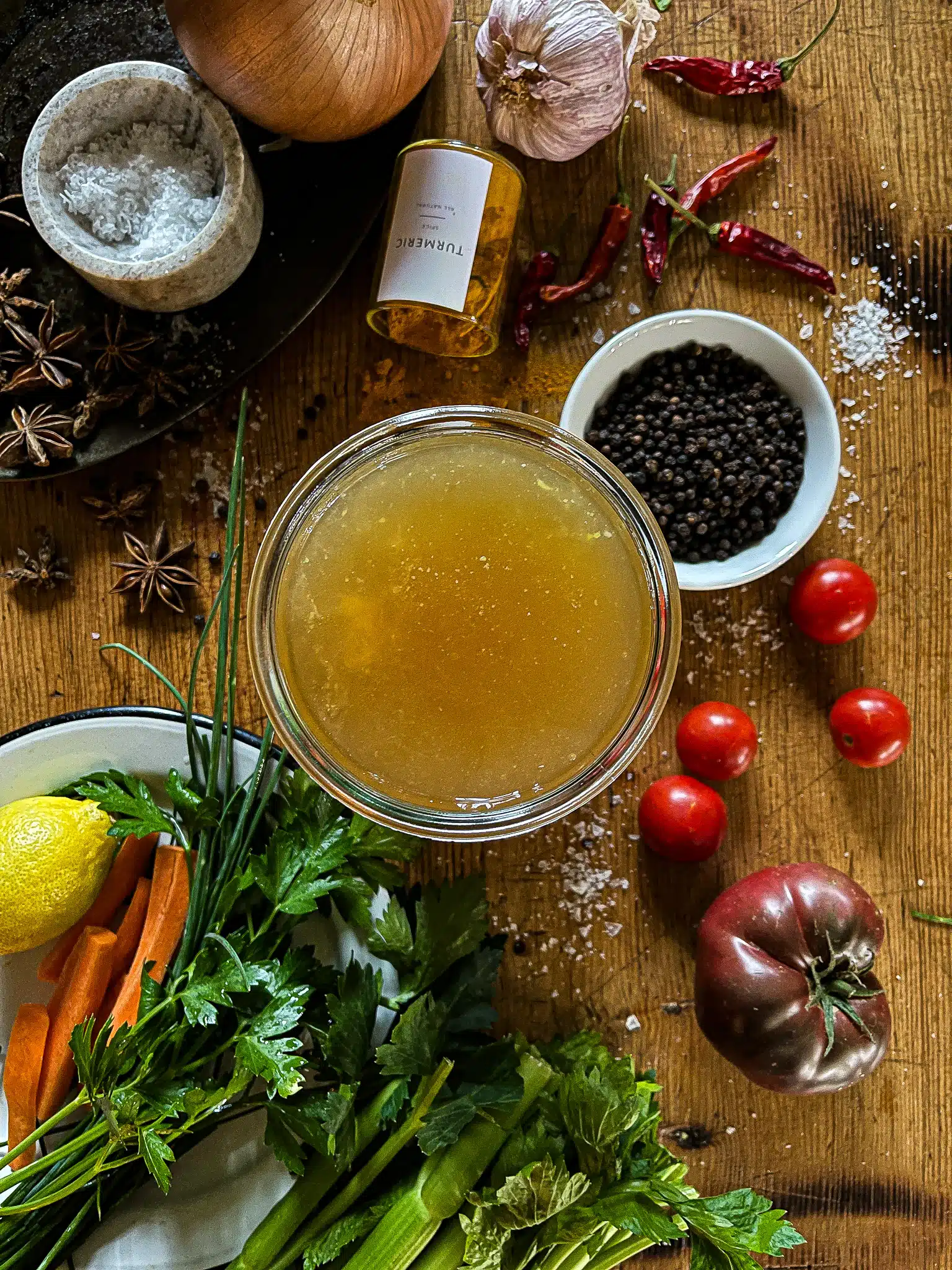 This is a picture of chicken bone broth in a weck jar flanked by bone broth ingredients like whole peppercorns, turmeric, and salt.