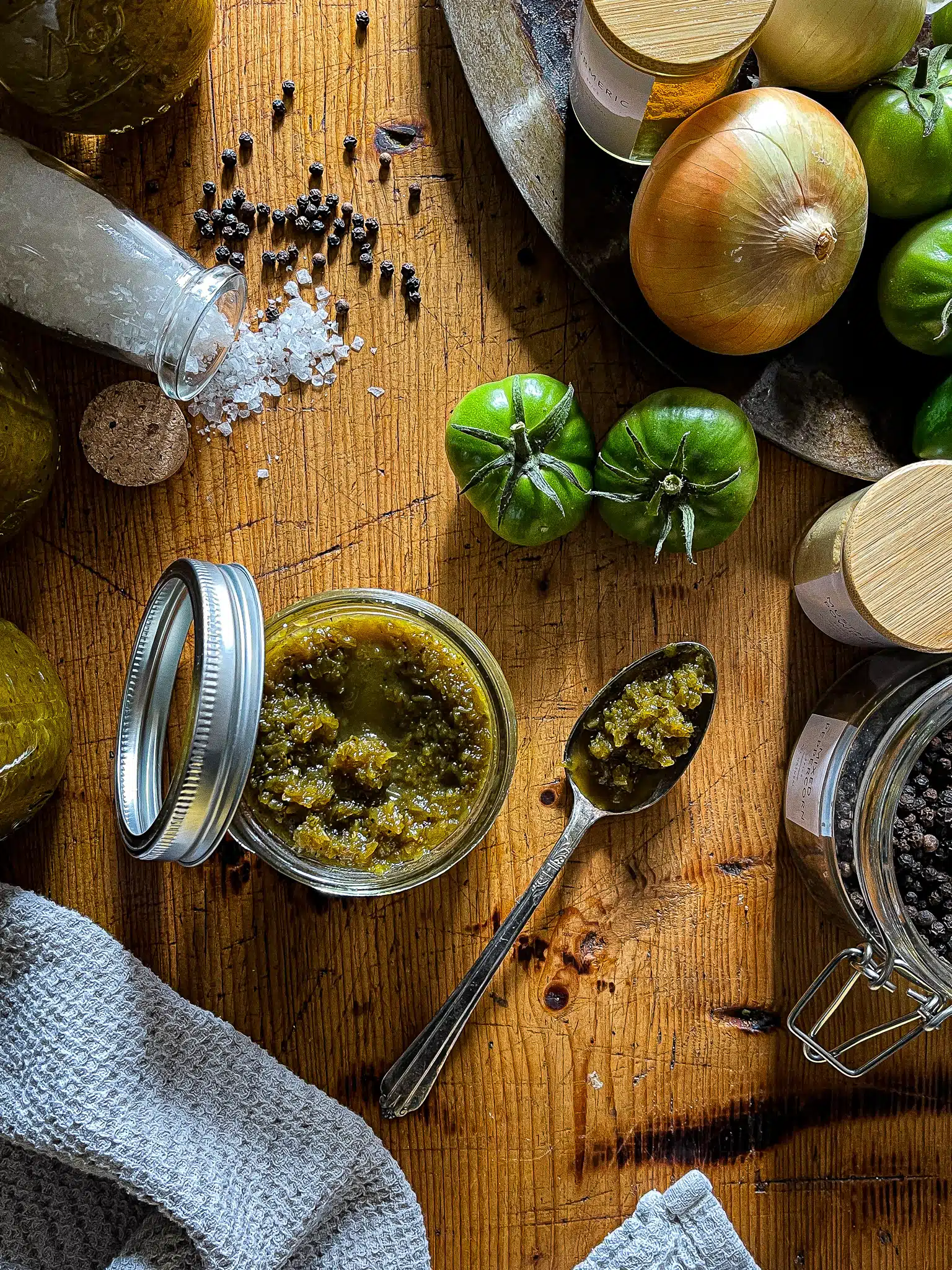 This is a picture of homemade chow chow raised over ingredients for the recipe. Green tomatoes, jalapeños, spices and salt and in the background.