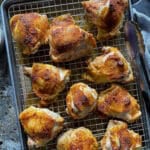 This is a picture of a sheet pan with baking rack topped with roasted chicken thighs.