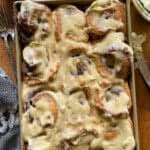 this is a picture of a baking pan of frosted cinnamon rolls sitting on a wooden background